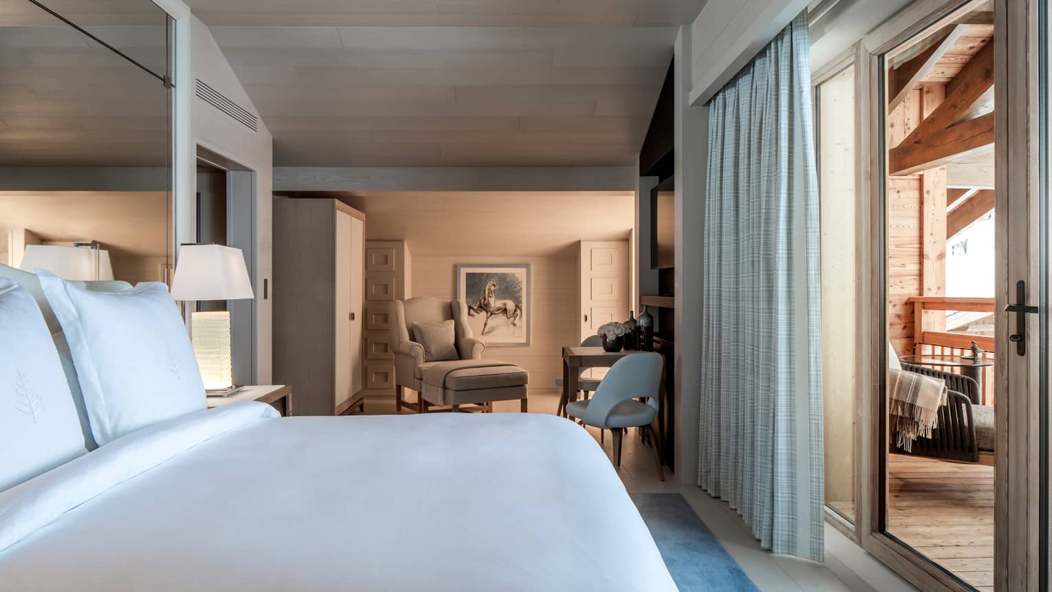 Junior Suite bed under mirror wall across from balcony doors, alcove with chair, table