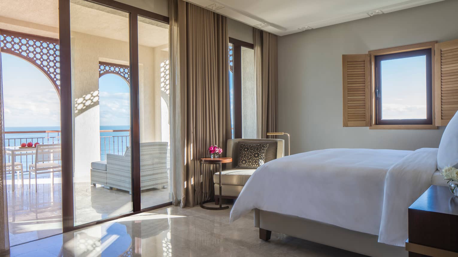 Mediterranean Suite bed with crisp white linens on gleaming marble floors by open patio doors