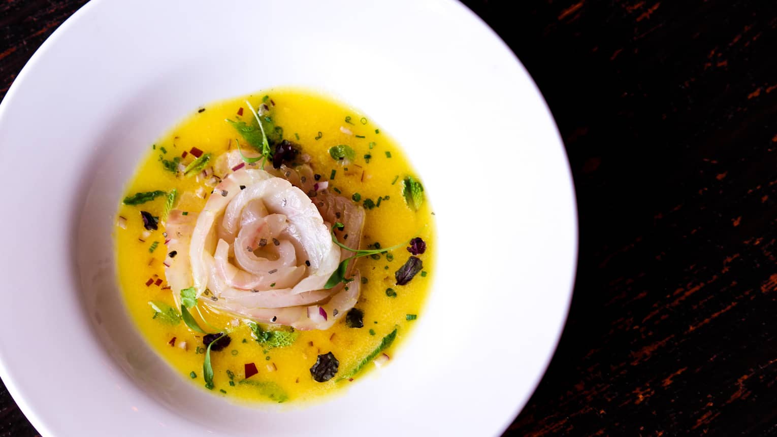 Rose-shaped ceviche in yellow sauce in large white bowl