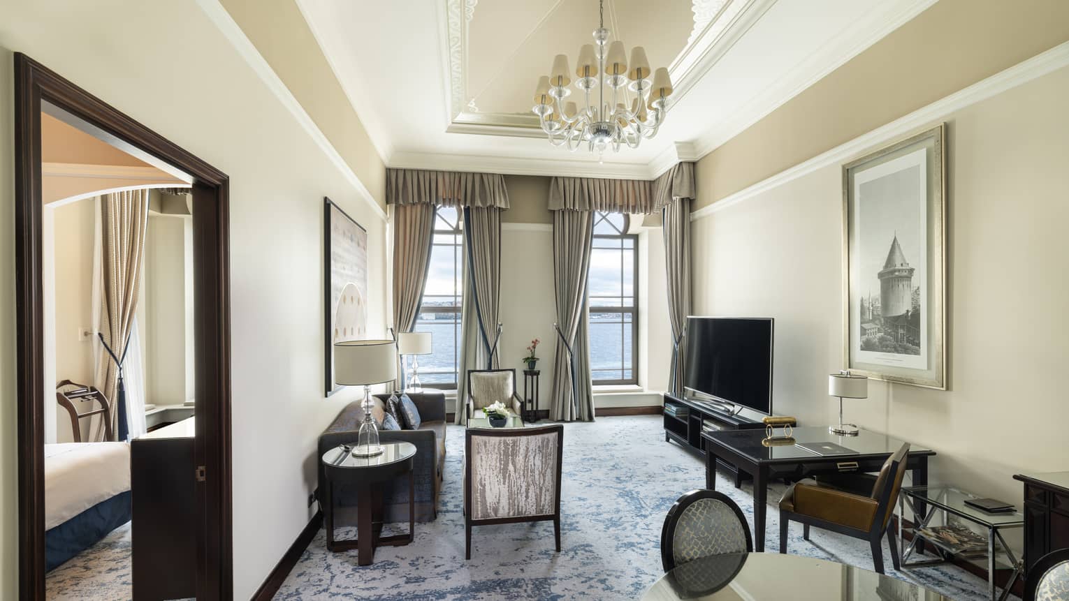 Elegant hotel suite living room featuring a chandelier, sofa, two chairs, TV and dining table