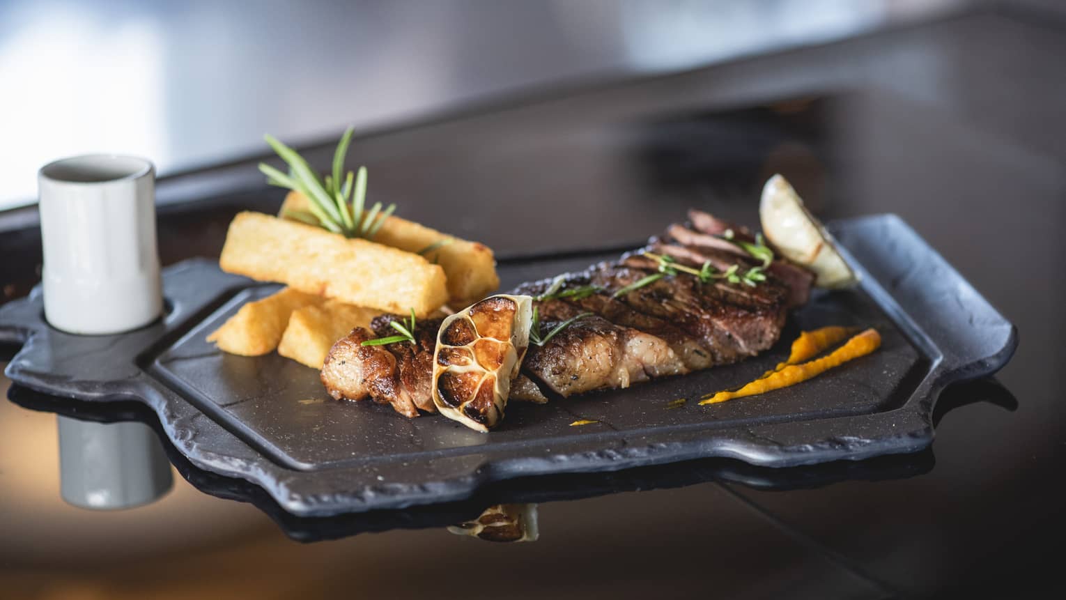 Grilled meat, lemon wedges with frites on slate platter