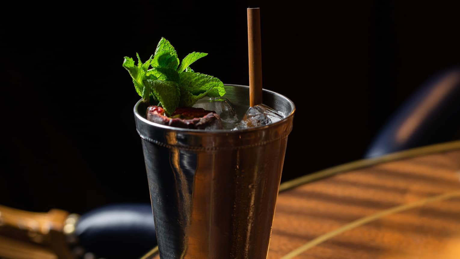 A cocktail with green herbs in a metal glass.