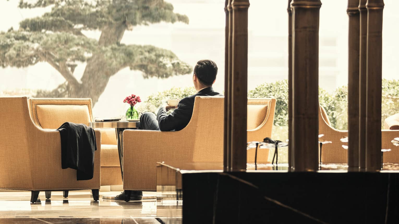 La Sala lounge, back of man in suit in upholstered armchair by small cocktail table