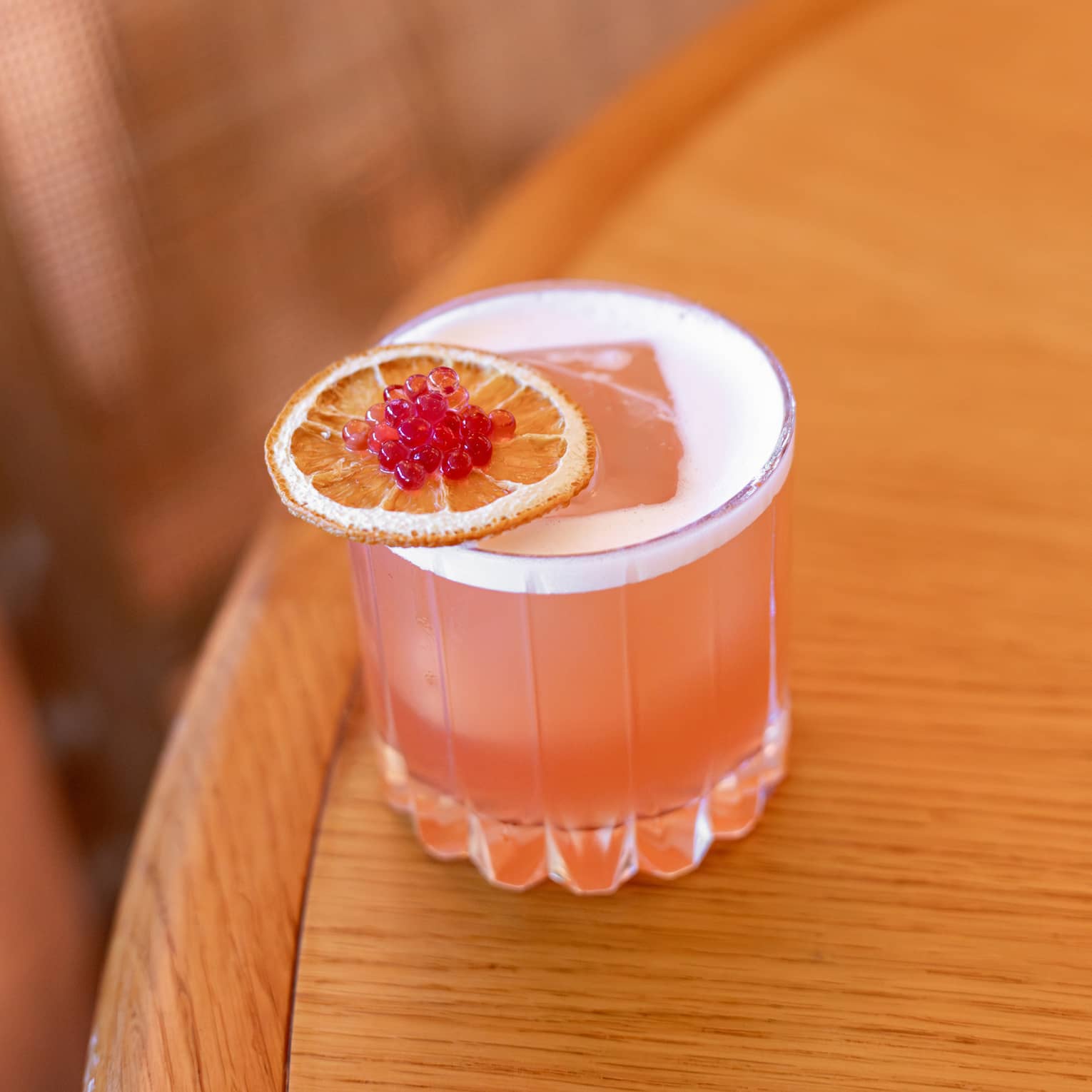 Coral-hued cocktail served in a rocks glass and garnished with an orange slice