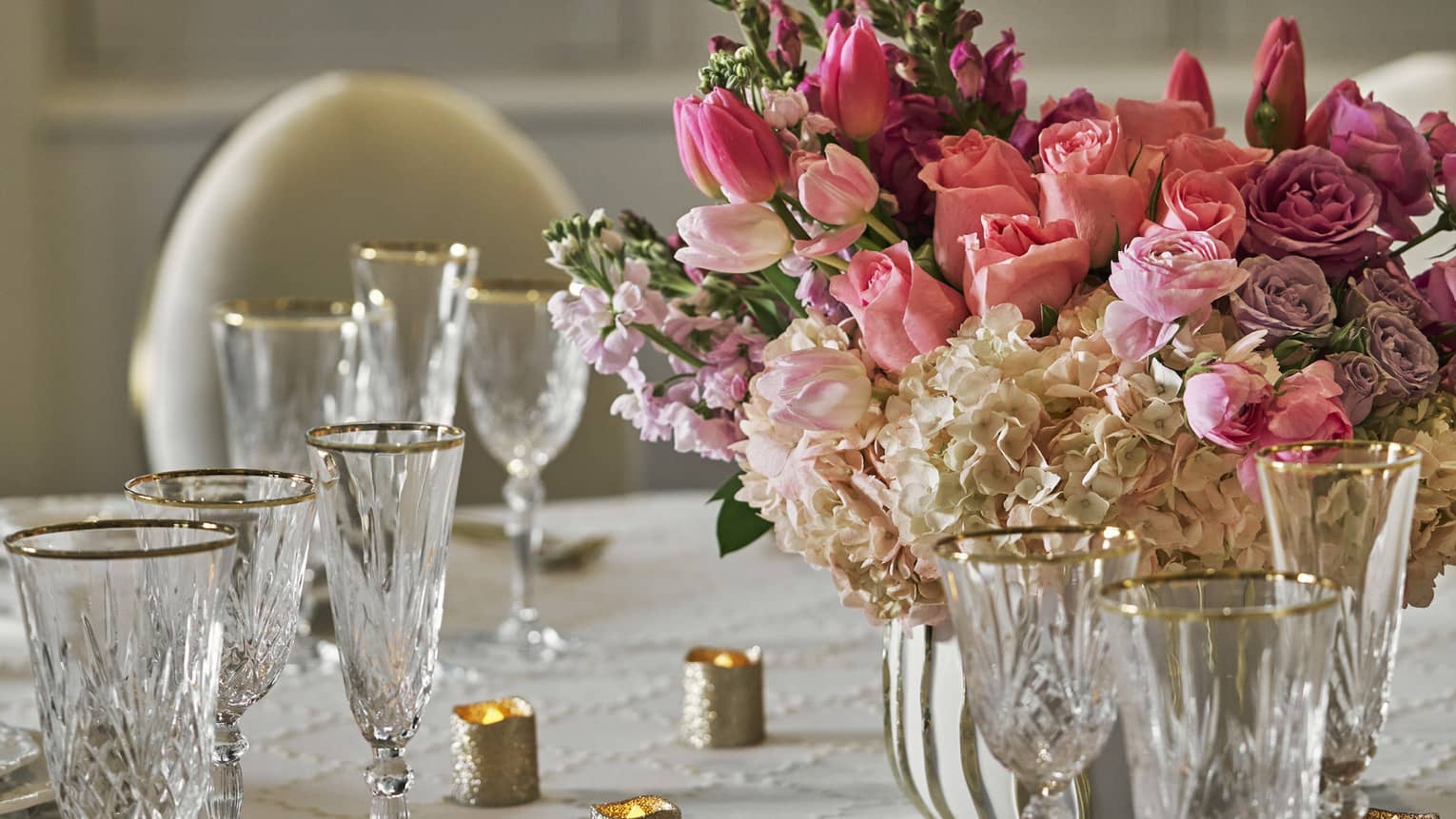 A banquet table set with fine dining tableware and a pink floral arrangement