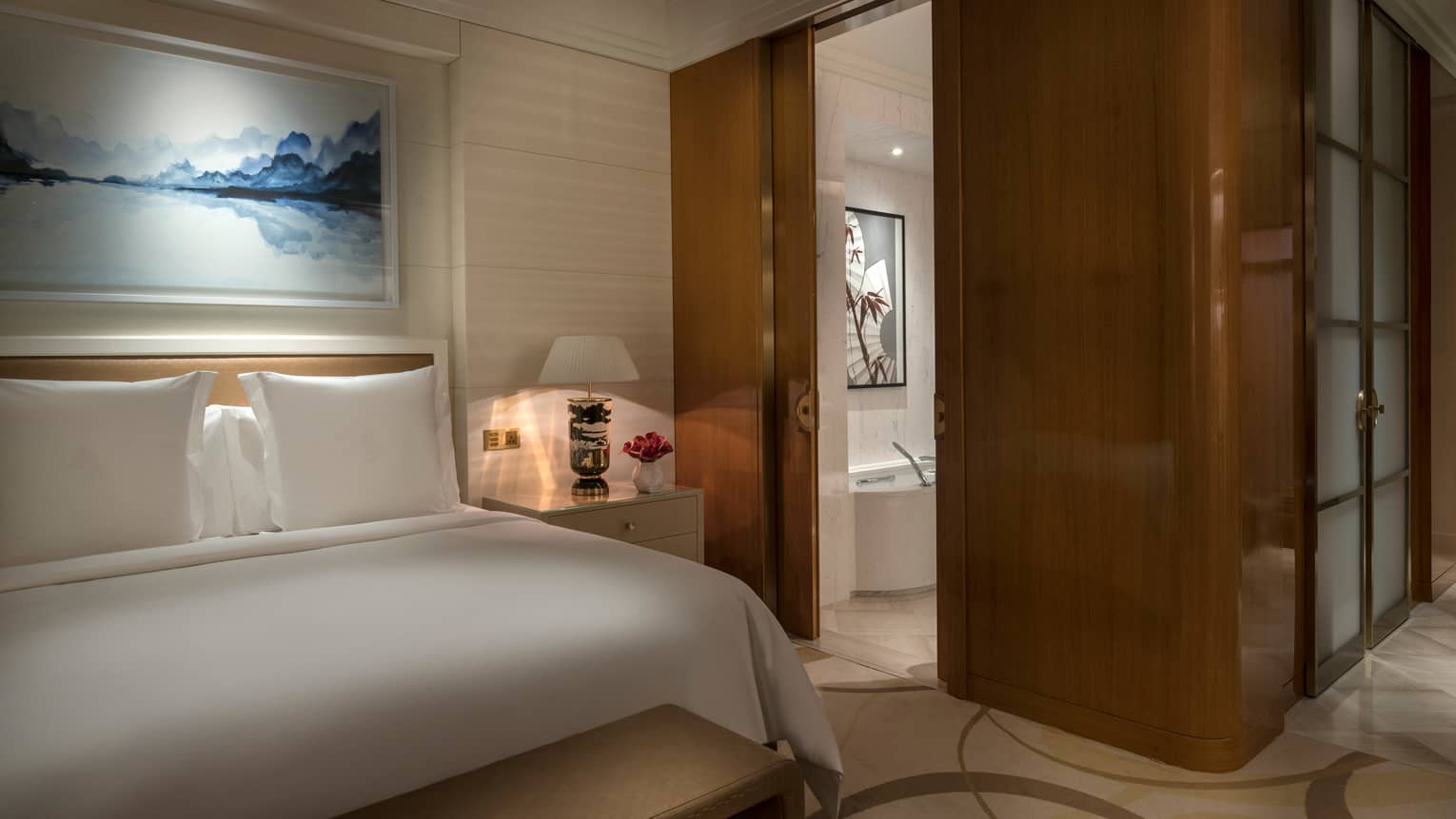 Custom King bed under blue-and-white painting, wood panel walls, sliding bathroom door