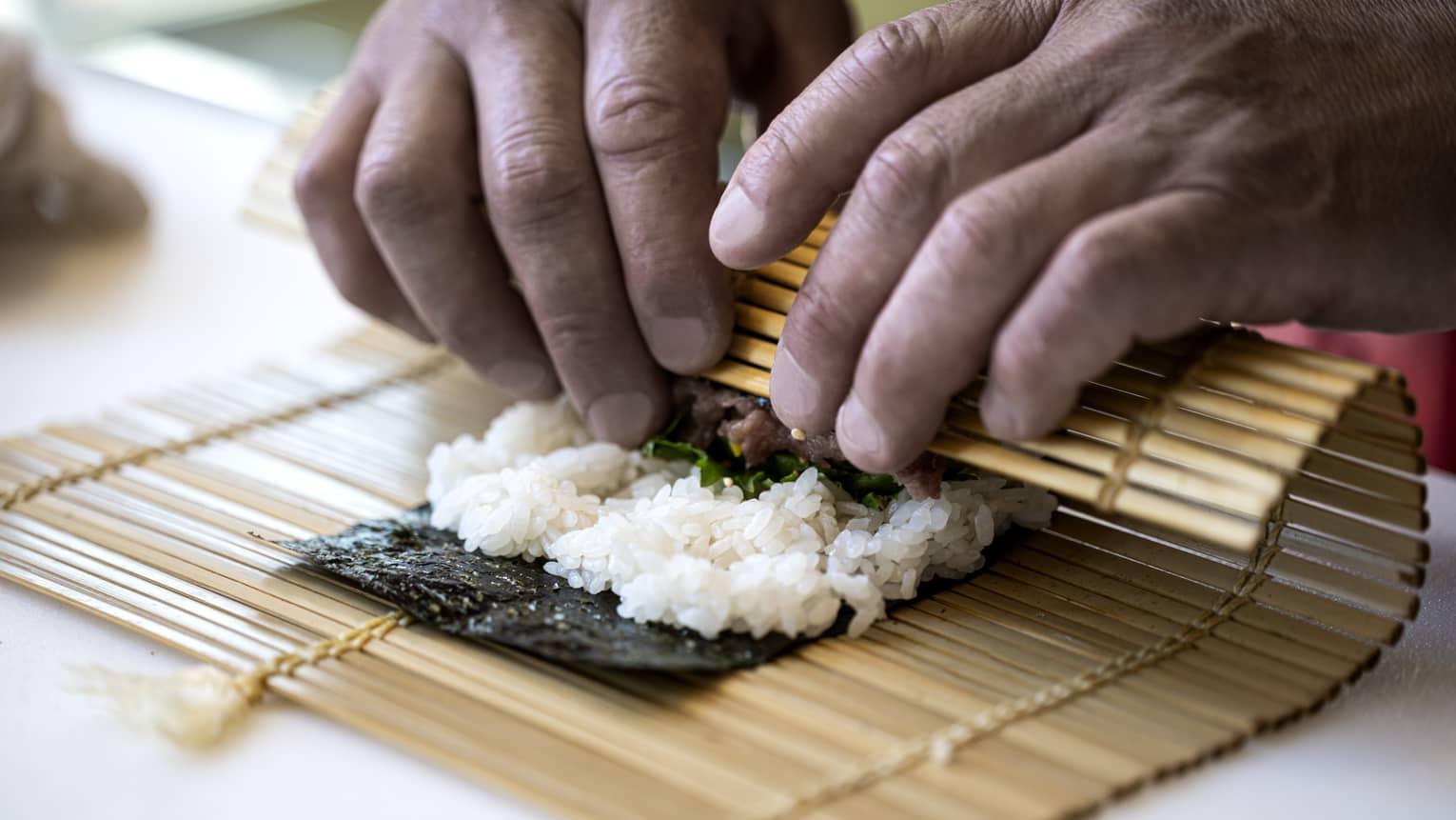 A four seasons chef rolls sushi with a bamboo mat