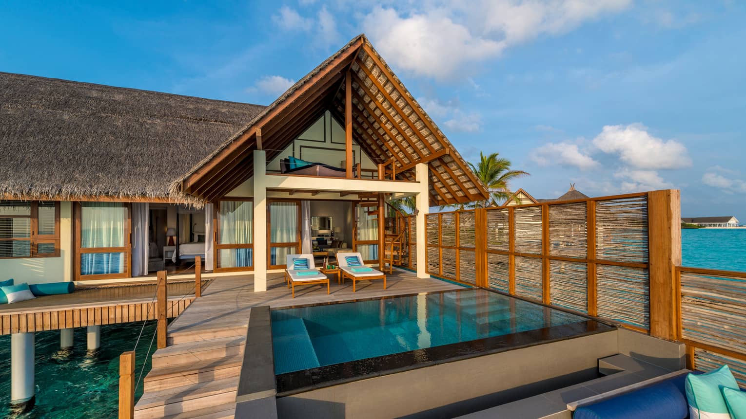 Sunset Water Villa with Pool patio chairs by plunge swimming pool under thatched roof