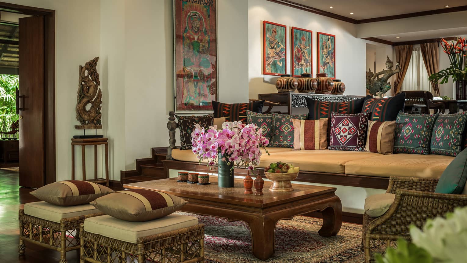 Residence living room with long sofa and two ottomans covered with Thailand textile pillows, wood table