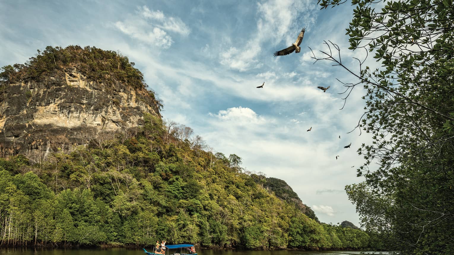 People on small blue boat on river under small rocky mountain