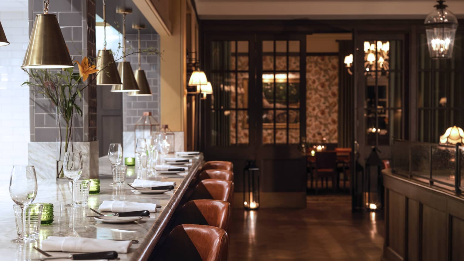 Long white marble dining bar with plates, cloth napkins, wine glasses, brown leather stools