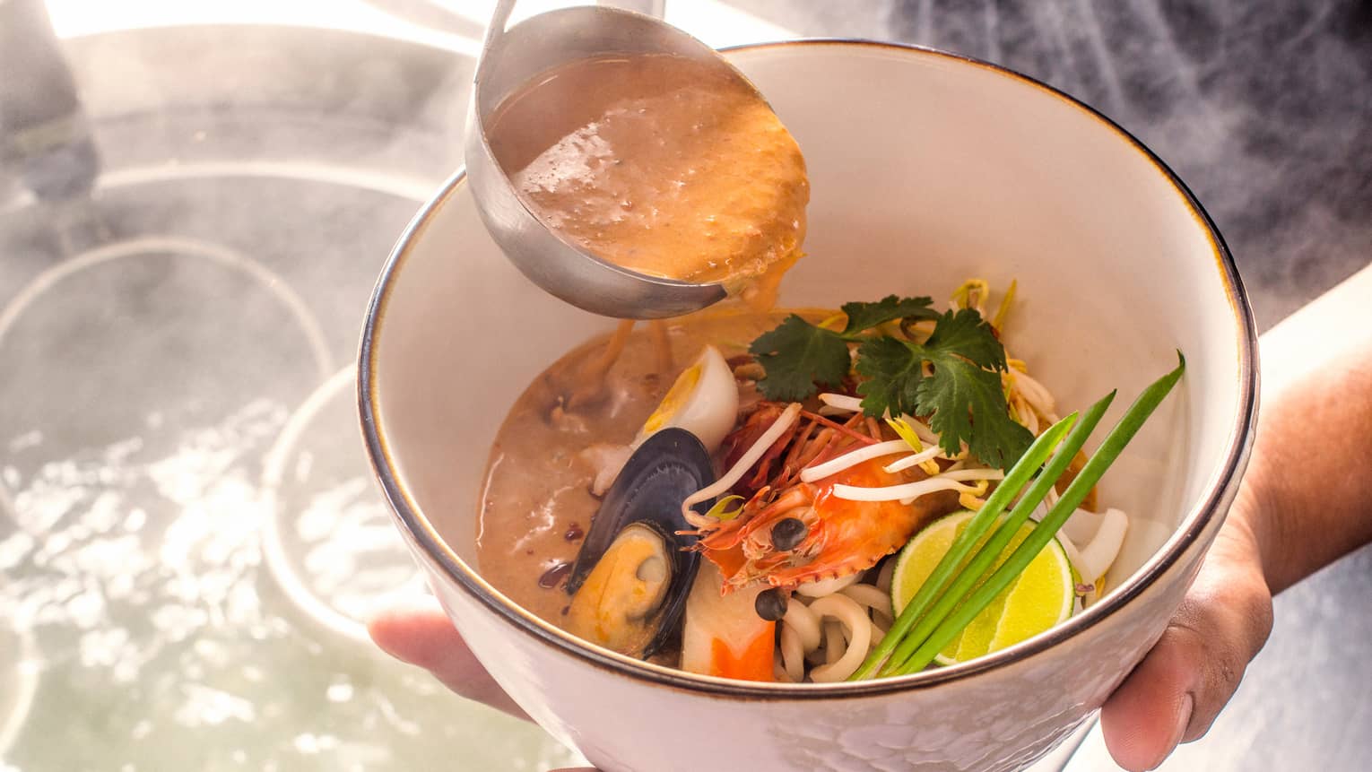 Close-up of hands holding Laksa Noodle seafood dish, ladle with sauce 