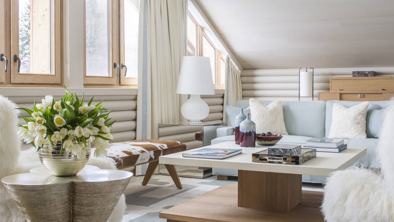Suite D'Arbois seating area with bright, white Alpine-chic décor, flowers, cowhide bench