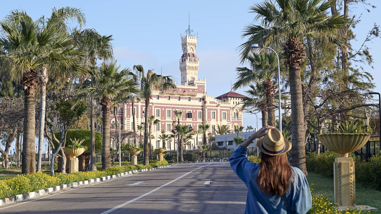 Rear view of a guest approaching a palatial structure with a tall, square tower stretching towards the clear, blue sky.