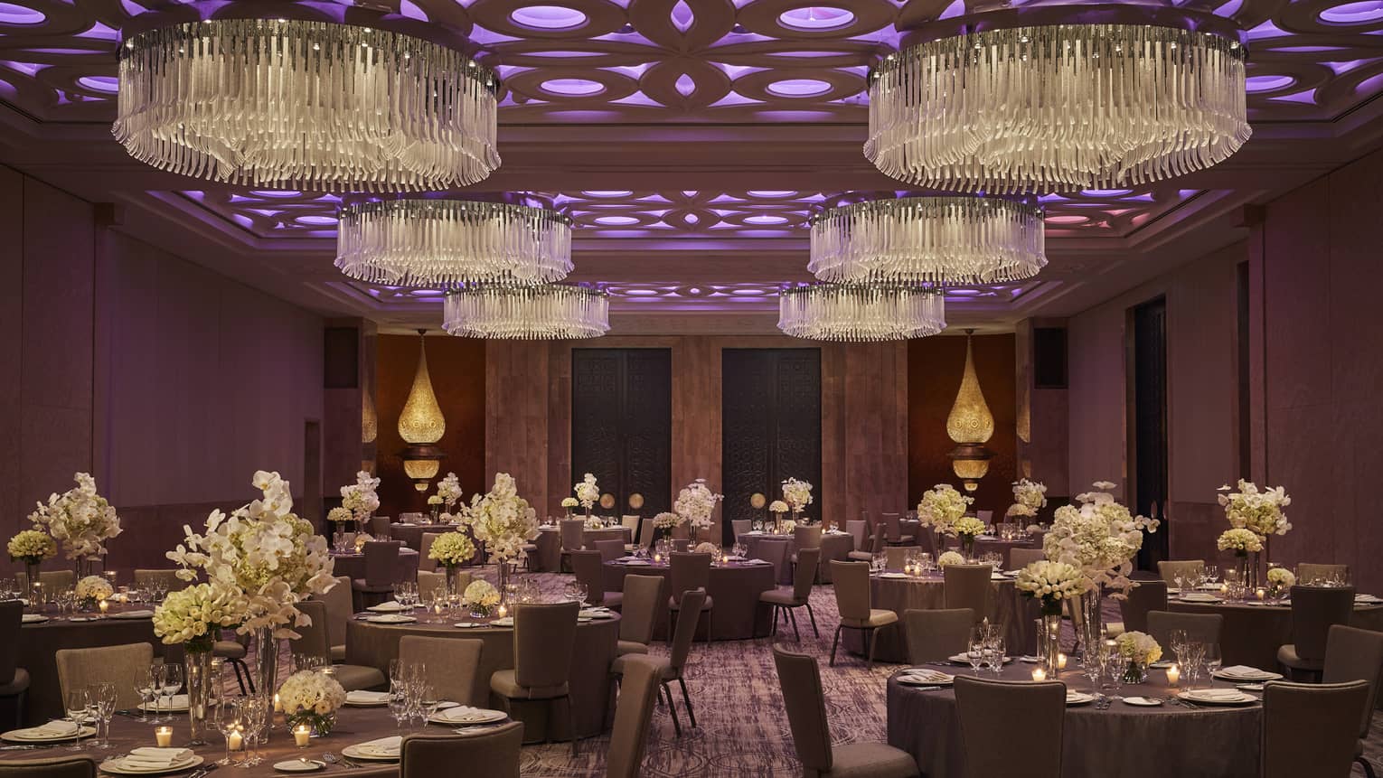 Round banquet dining tables in ballroom with round chandeliers, purple lights on ceiling