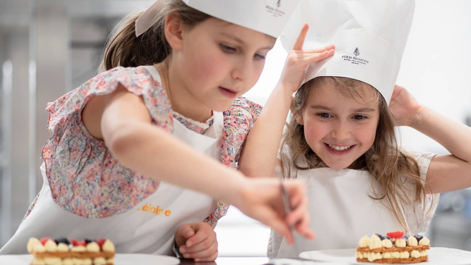 Two young children wearing Four Seasons chef hats work on dessert creations at a cooking class in a Four Seasons kitchen