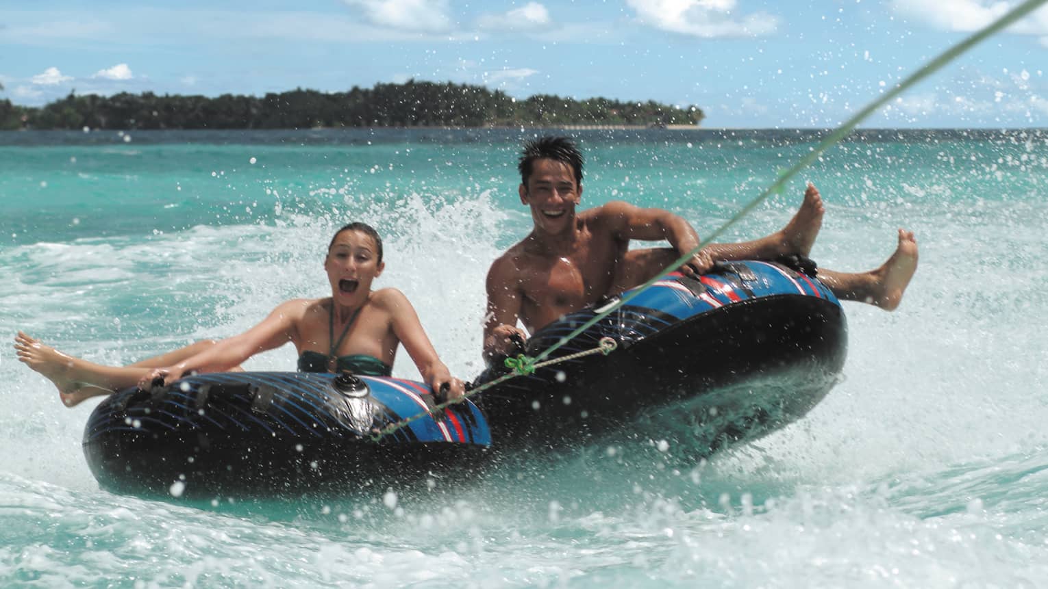 Laughing man and woman hold onto inflatable inner tubes as they ride on ocean