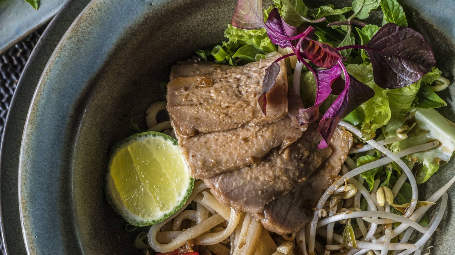 Wagyu Beef Tomahawk on noodles with green lettuce, lime