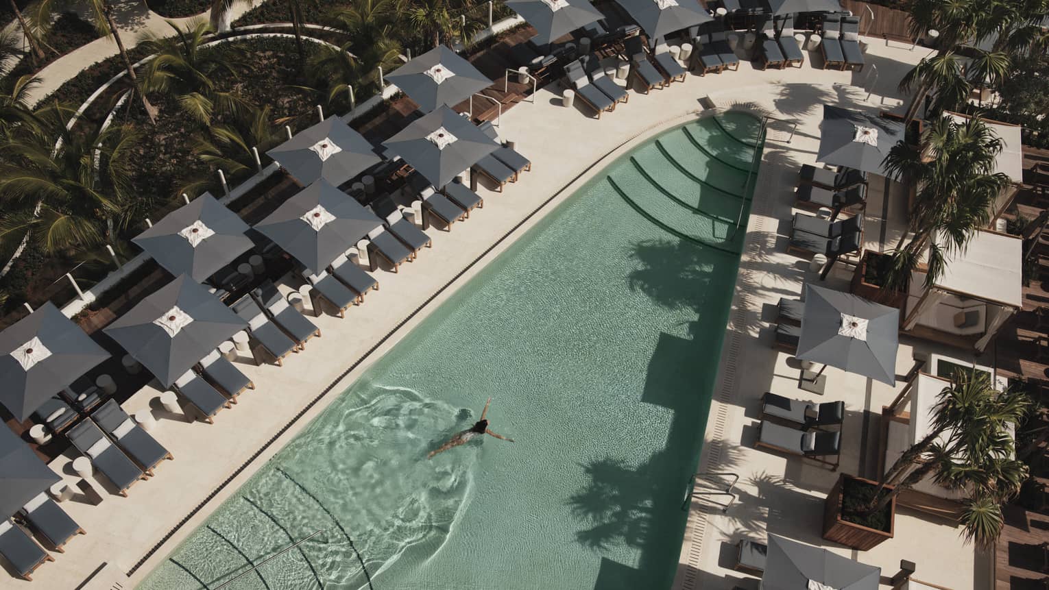Aerial view of an outdoor pool surrounded by grey lounge chairs and umbrellas, creating a relaxing atmosphere.