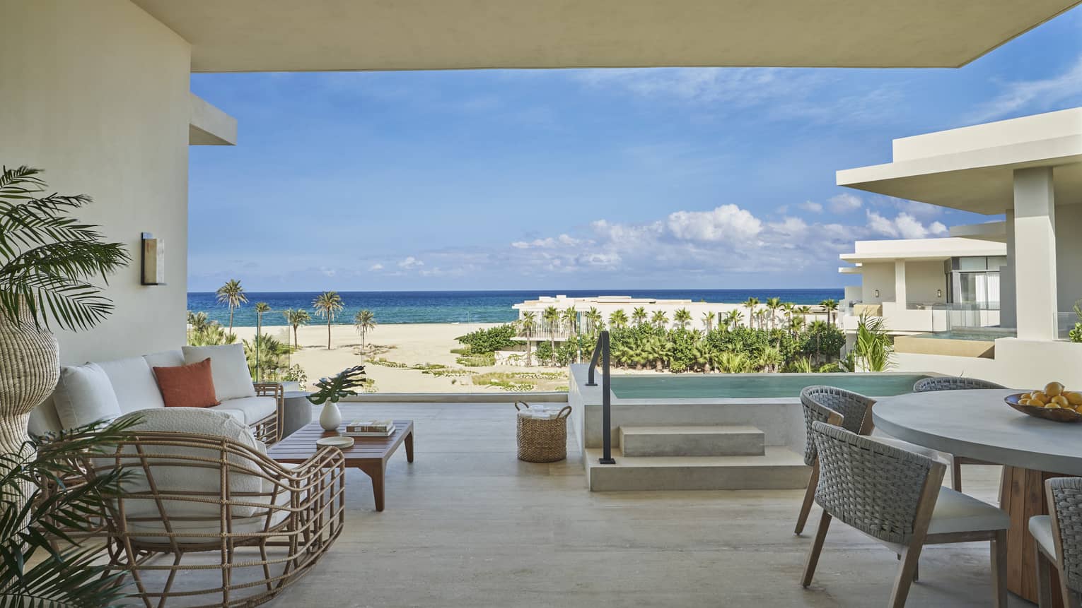 Modern terrace with white seating vignette, dining table, steps up to private pool, and beachfront view