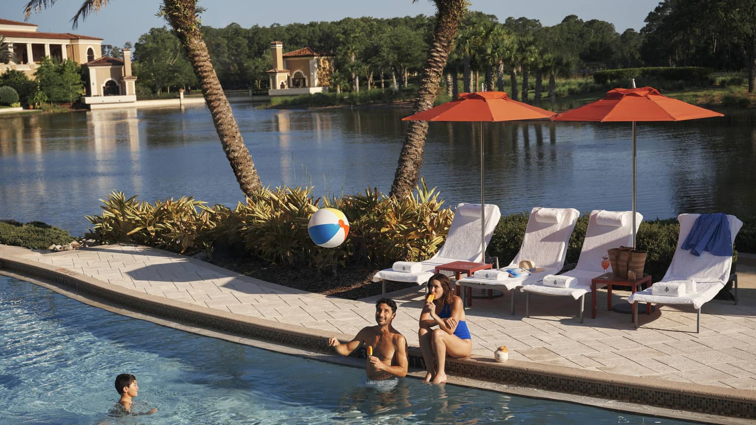 Two adults play with kid and a beach bar in the family pool at luxury resort