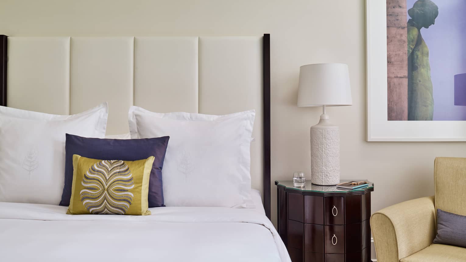 Close-up of Superior Room bed with white padded headboard, blue and gold accent pillows, lamp