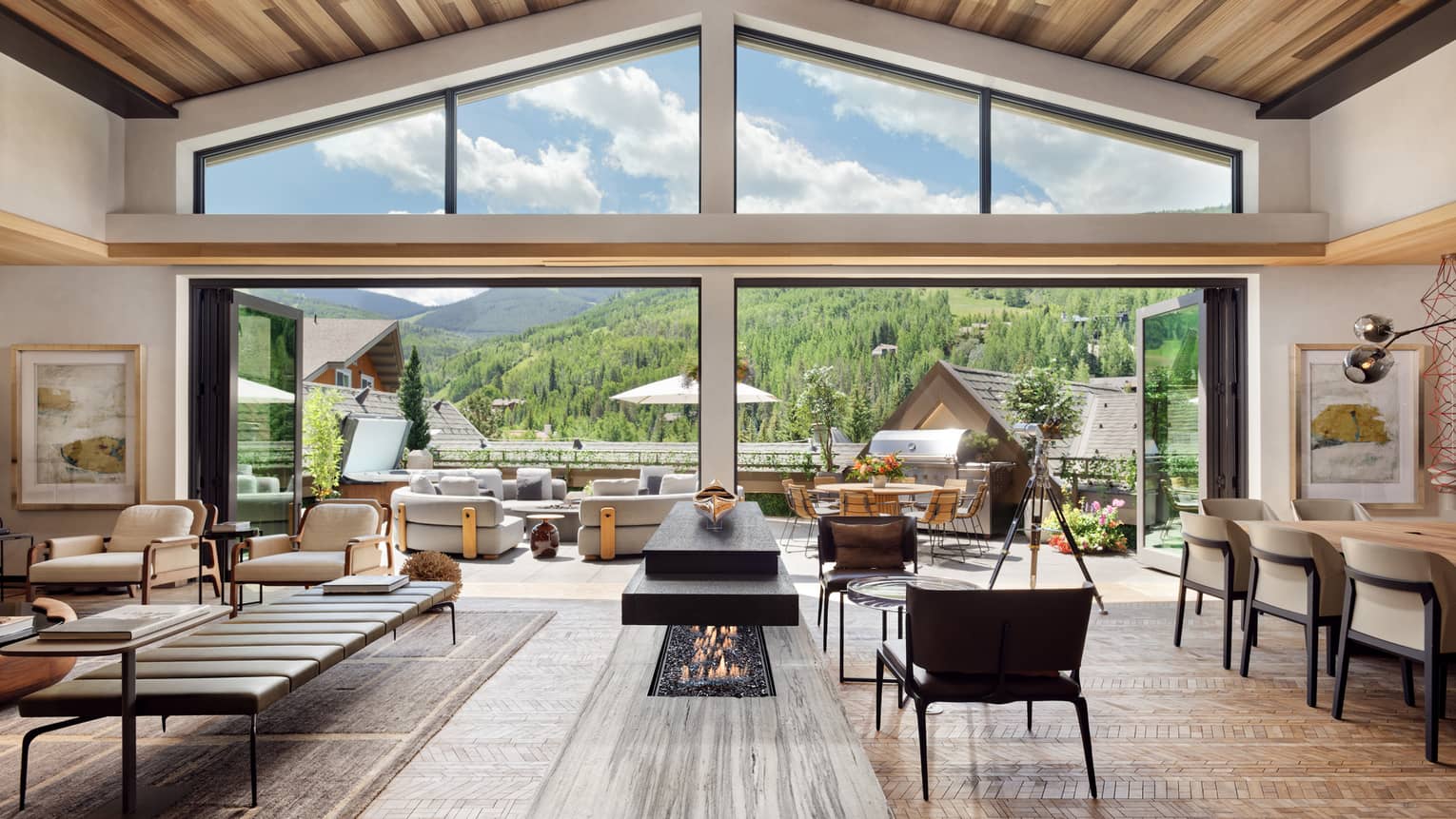Luxurious mountain villa interior with an open-plan living area, modern fireplace, and expansive glass doors leading to an outdoor terrace with panoramic forest views.
