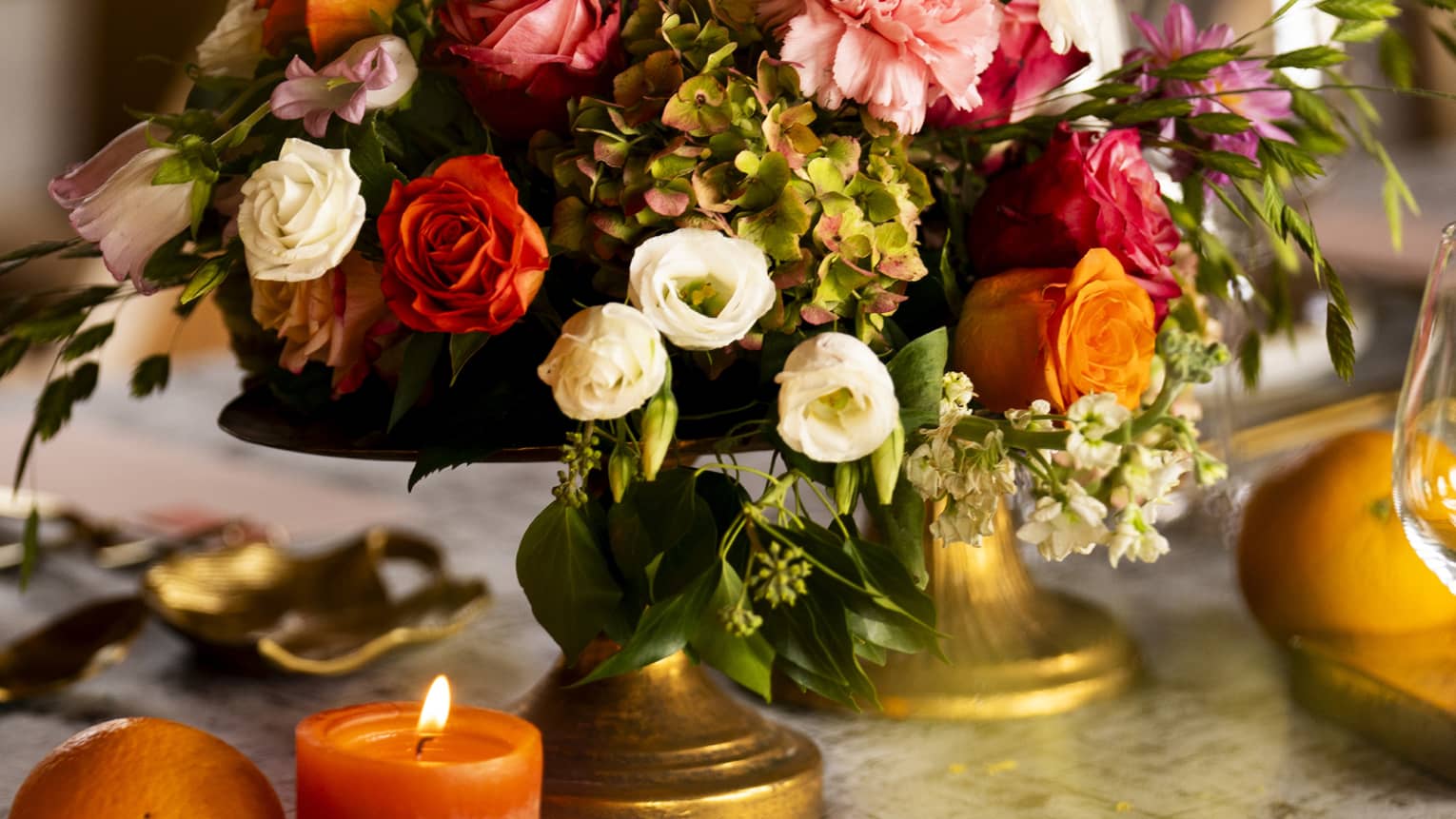 Bouquet of assorted autumn-coloured flowers with burnished pillar candles beside it