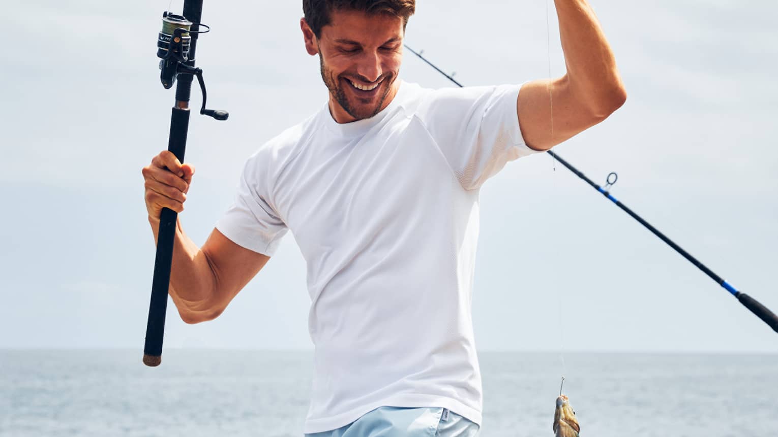A man near the ocean holding a fishing line with a fish caught on it.