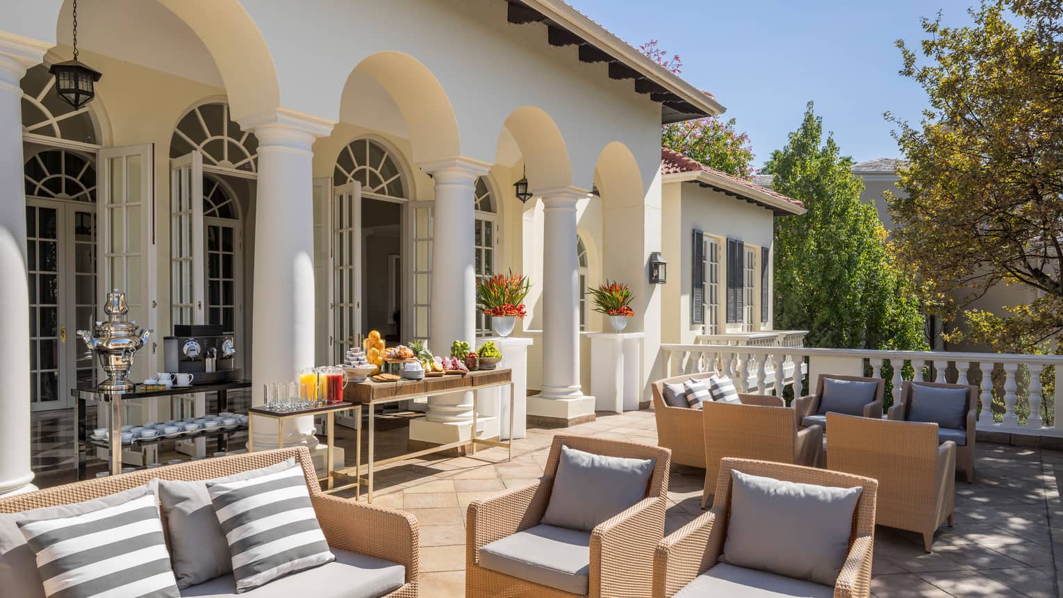 White pillars, exterior behind sunny patio with breakfast buffet, wicker furniture with plush cushions