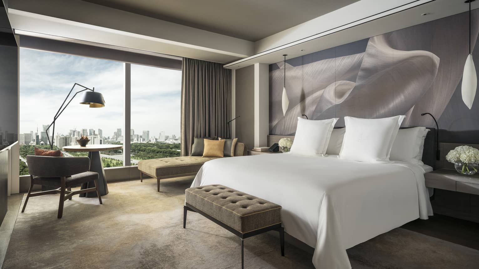 Hotel room with a cushioned bench at the end of white king bed and a wall of windows