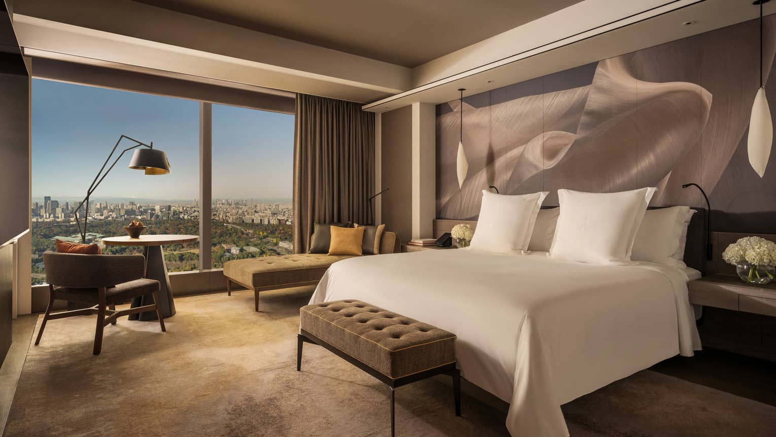 Hotel room with a cushioned bench at the end of white king bed and a wall of windows