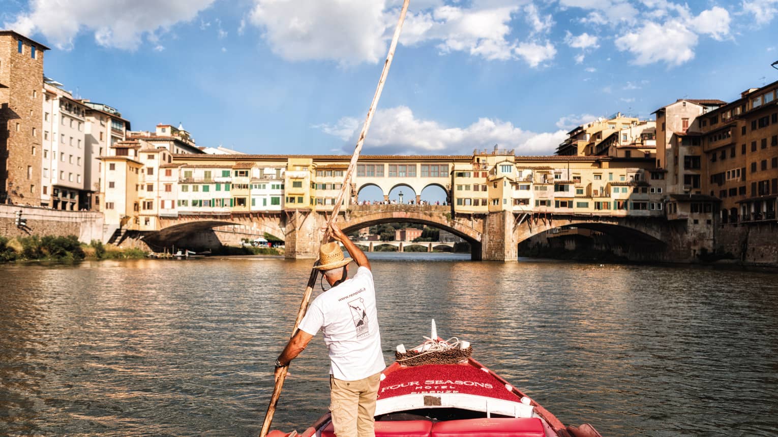 Man with long paddle steers Barchetto boat on Florence canal near bridge