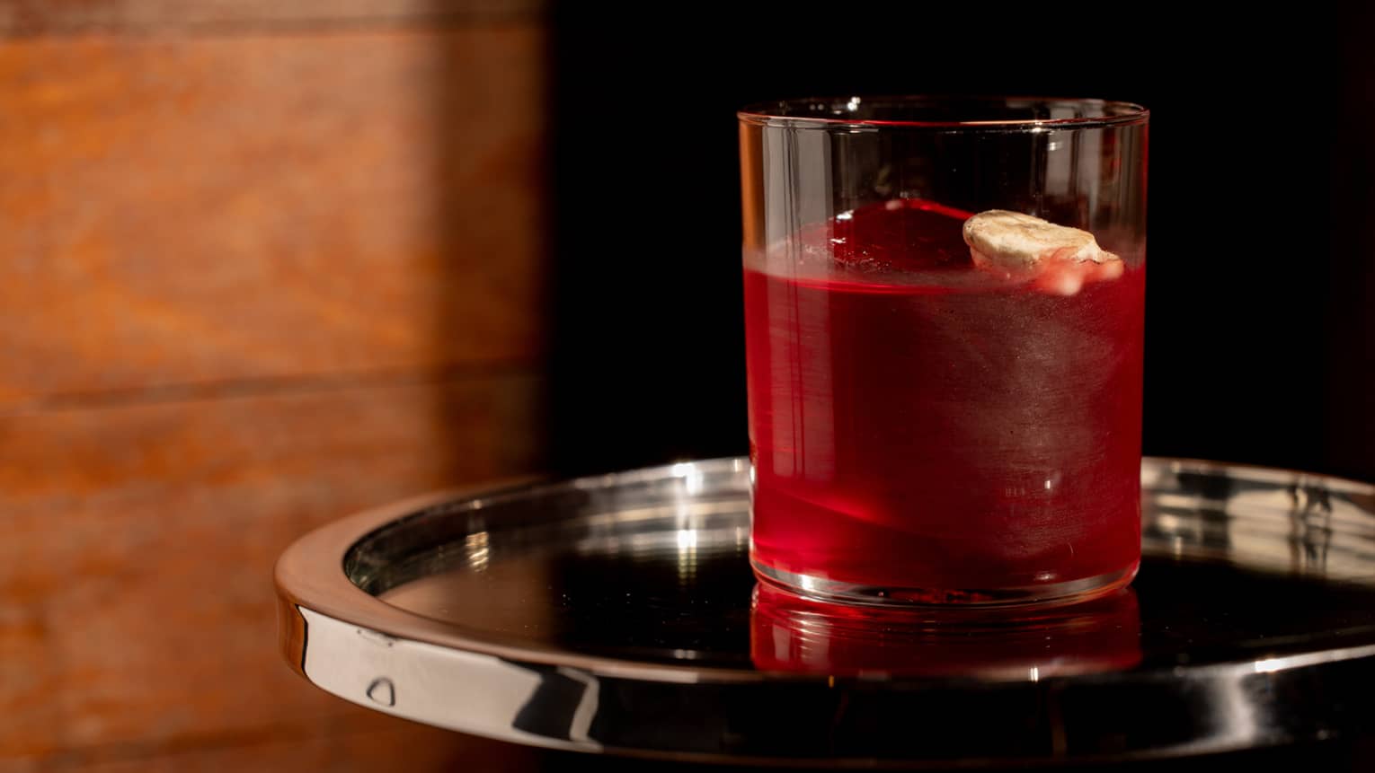 Dark-red-coloured mocktail in a rocks glass served on a silver tray