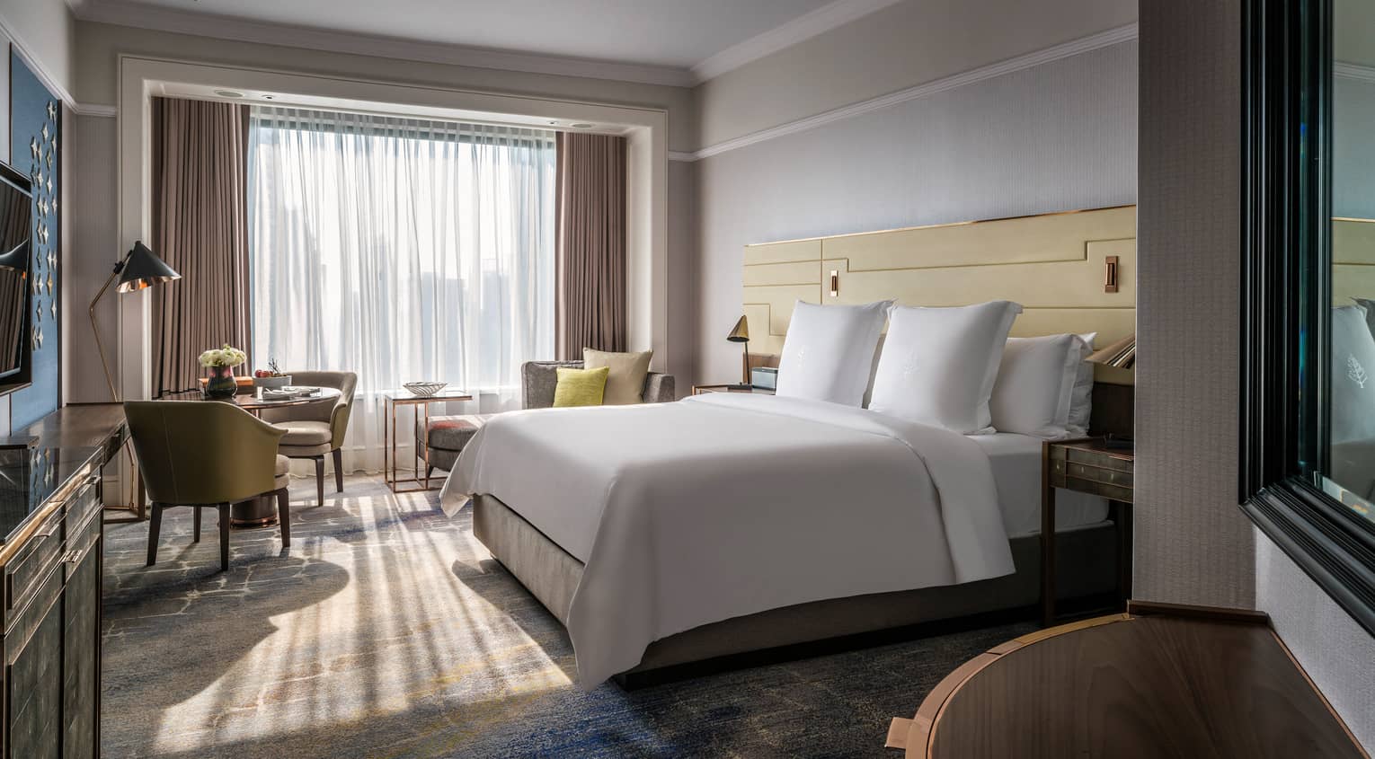 Sunny Premier Room bed with white linens, small dining table and chaise lounge, white curtains