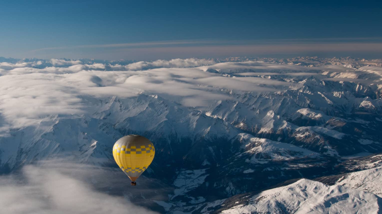 Yellow hot air balloon soaring over the snow-covered Alps