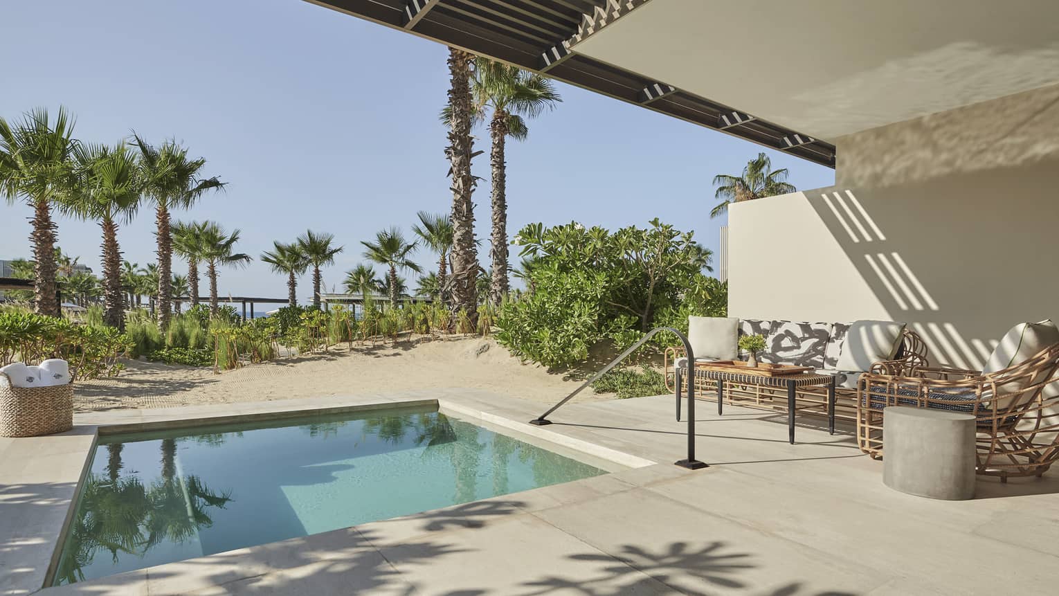Two Bedroom Ocean View Suite pool with rattan sofa and chair, palm trees, basket of beach towels