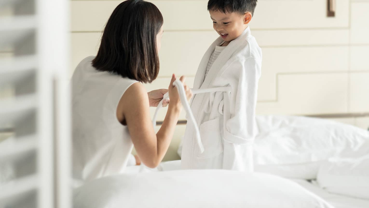 Woman kneels in front of young child, ties front of his white bathrobe