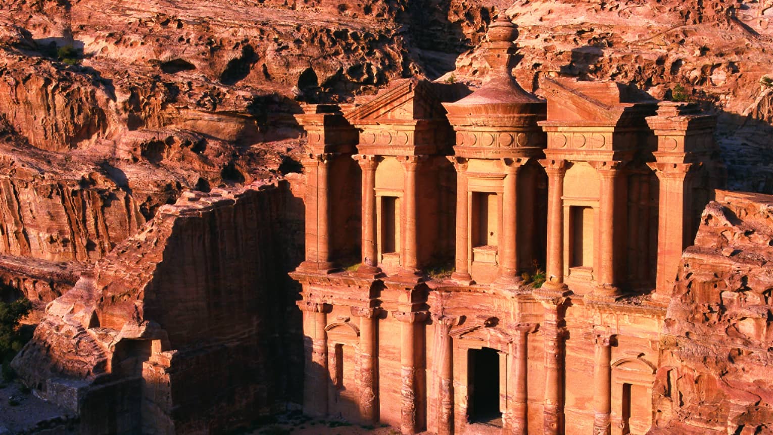 Sunlight across Petra ancient buildings carved into red rock 