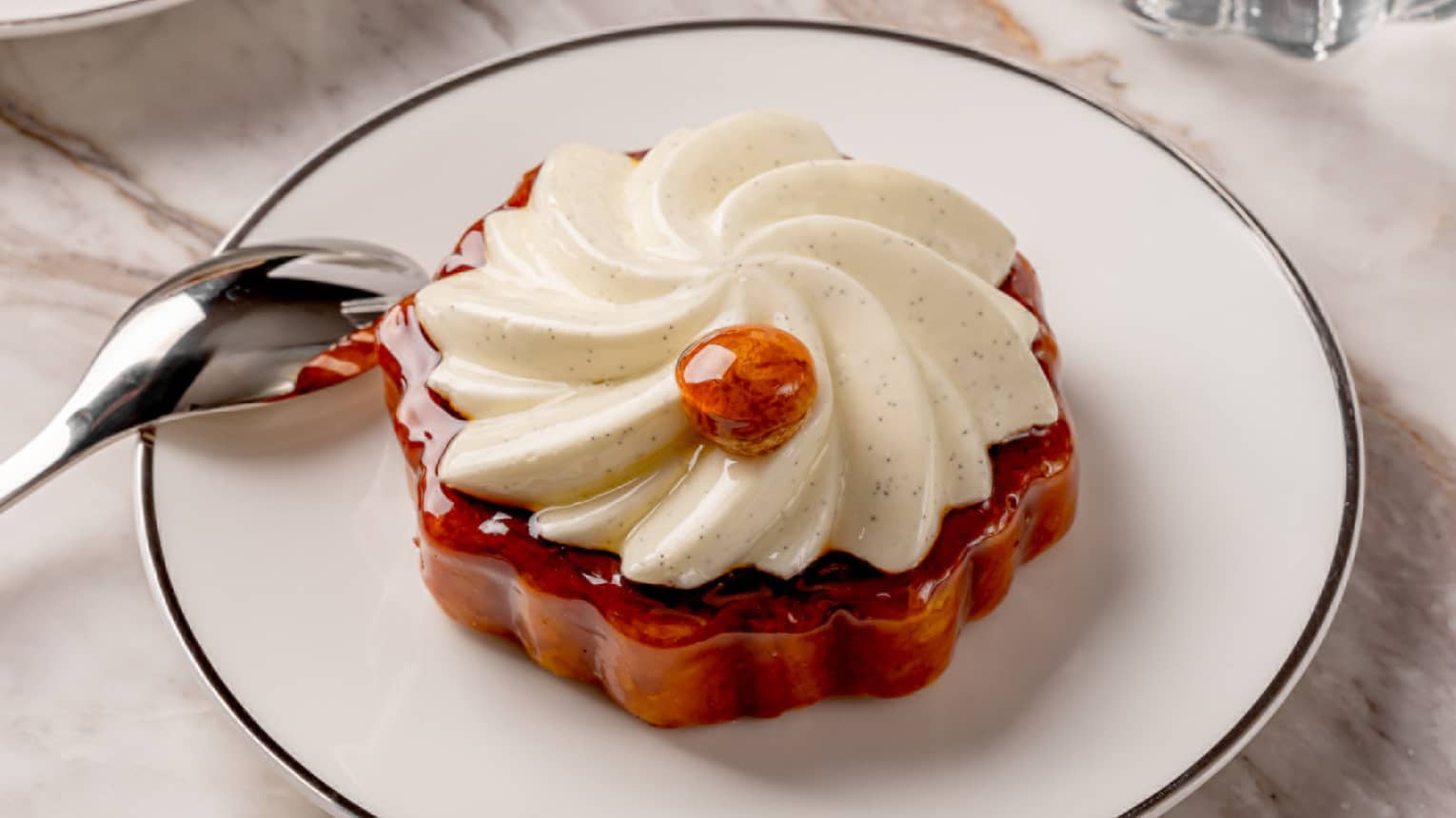 St Honor� pastry on a white round plate with a silver spoon perched on the edge and a glass of water and cup of espresson nearby