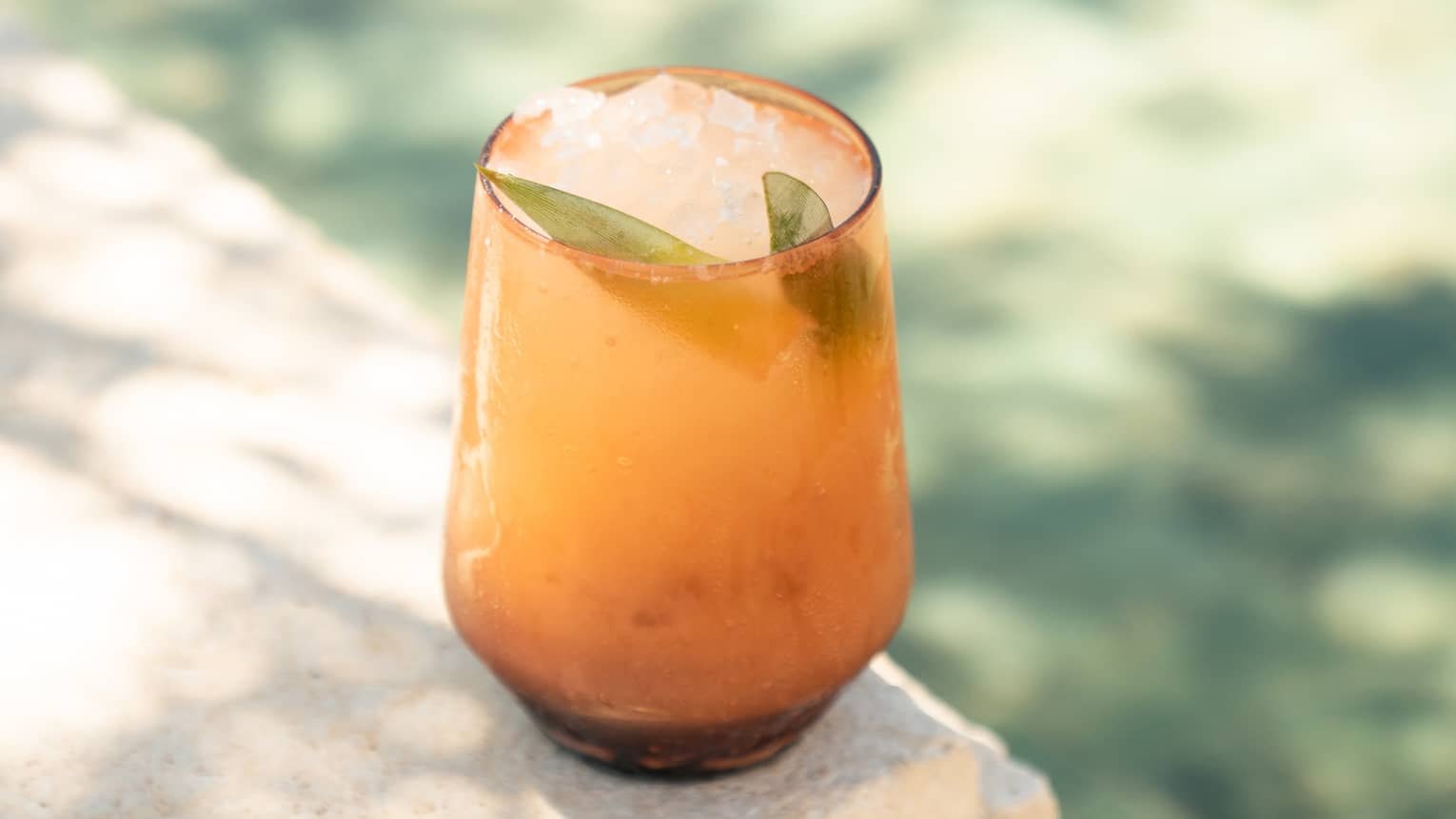 A tumbler with a garnished cocktail in an outdoor setting
