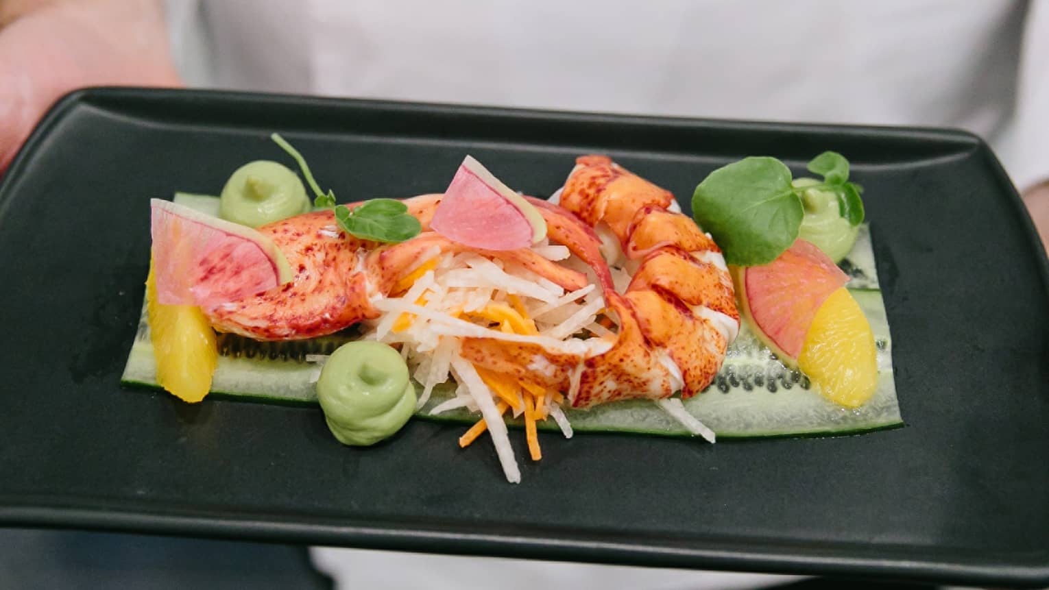 A chef holing a black tray of seafood and fruit.