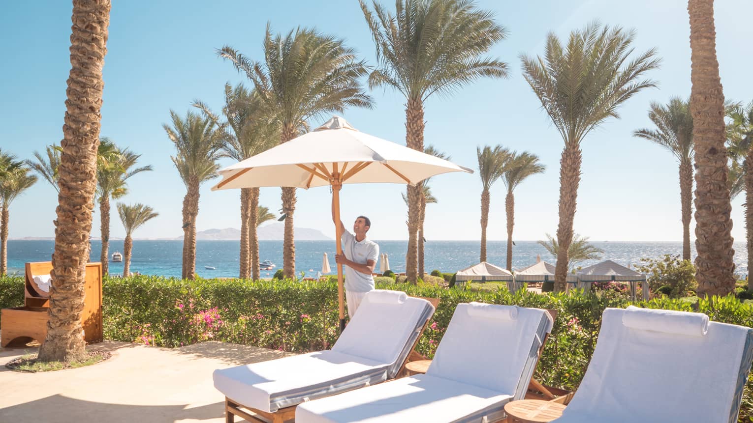 Sun chairs on pool deck, man opening sun umbrella, sea in distance