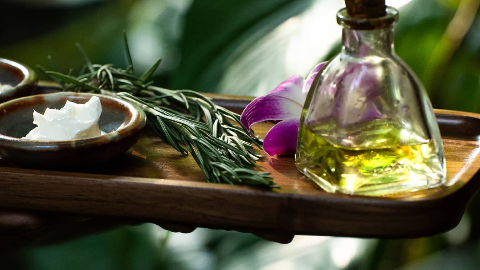 Spa oil, lotion and herbs on wooden tray in garden setting