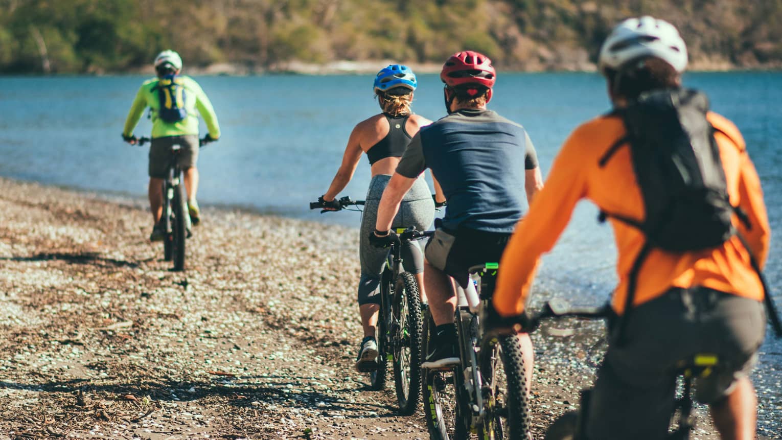 Four people riding bicycles through a rocky terrain next to the ocean