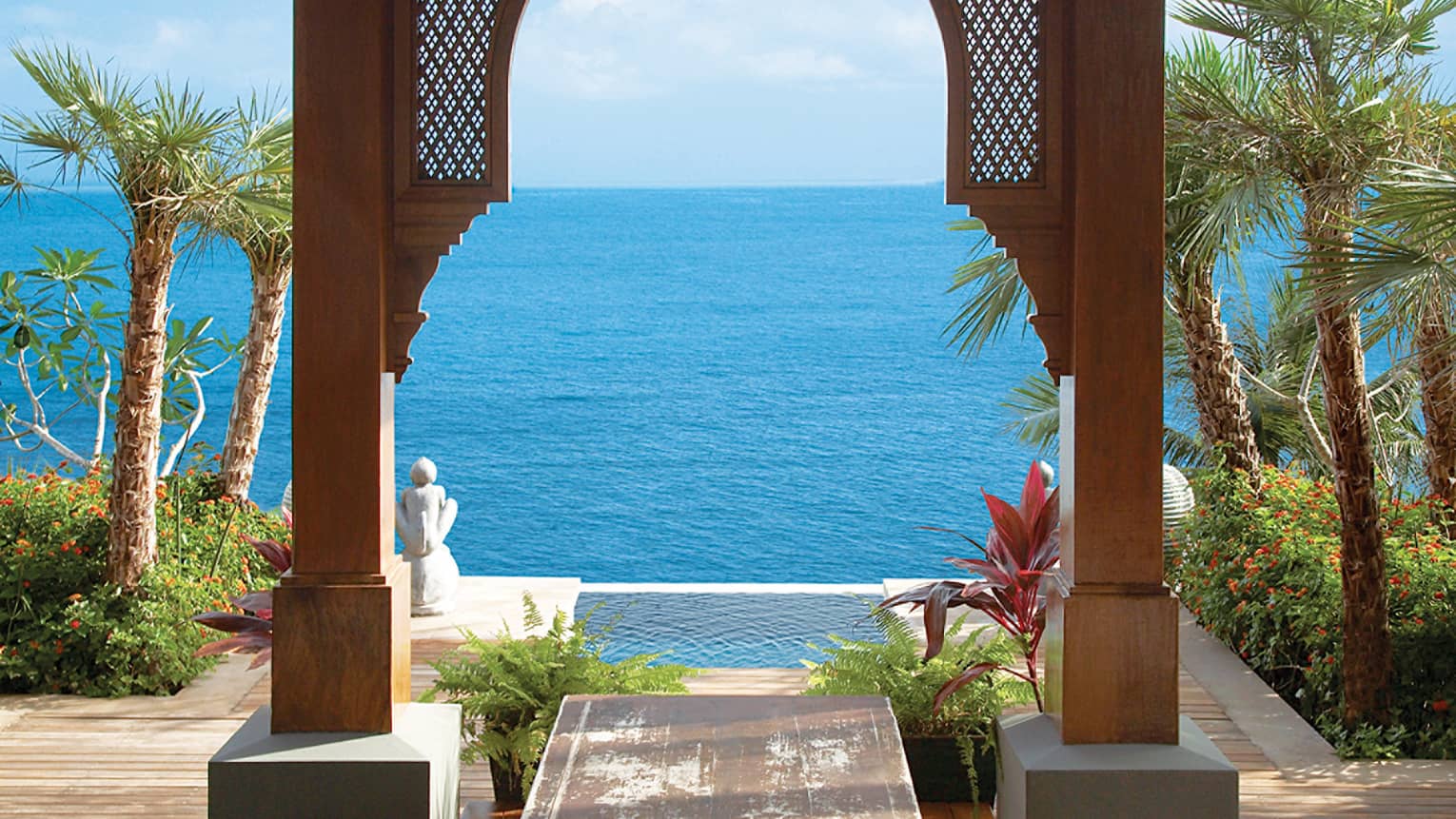 Wood archway, pool palms and ocean under blue sky