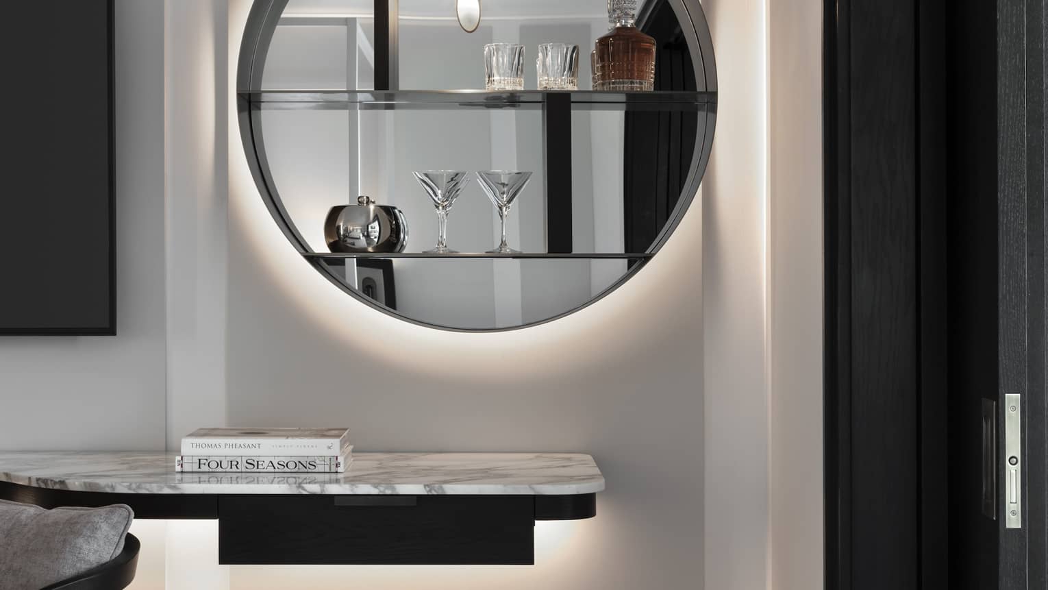 In-room bar with round modern mirror and cocktail glasses on shelves
