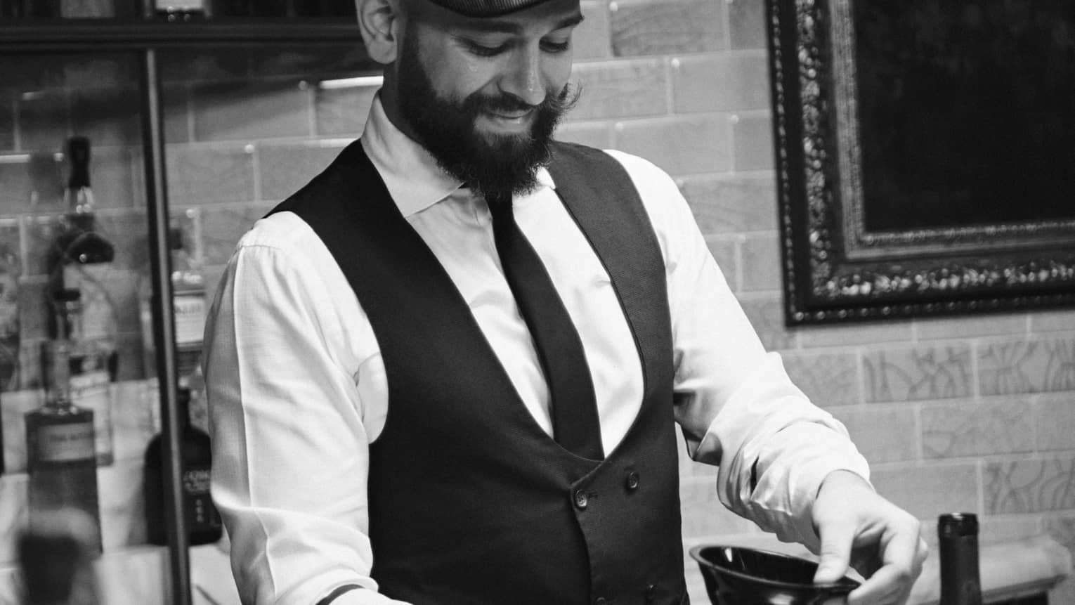 A bartender wearing a tie and vest works behind a bar