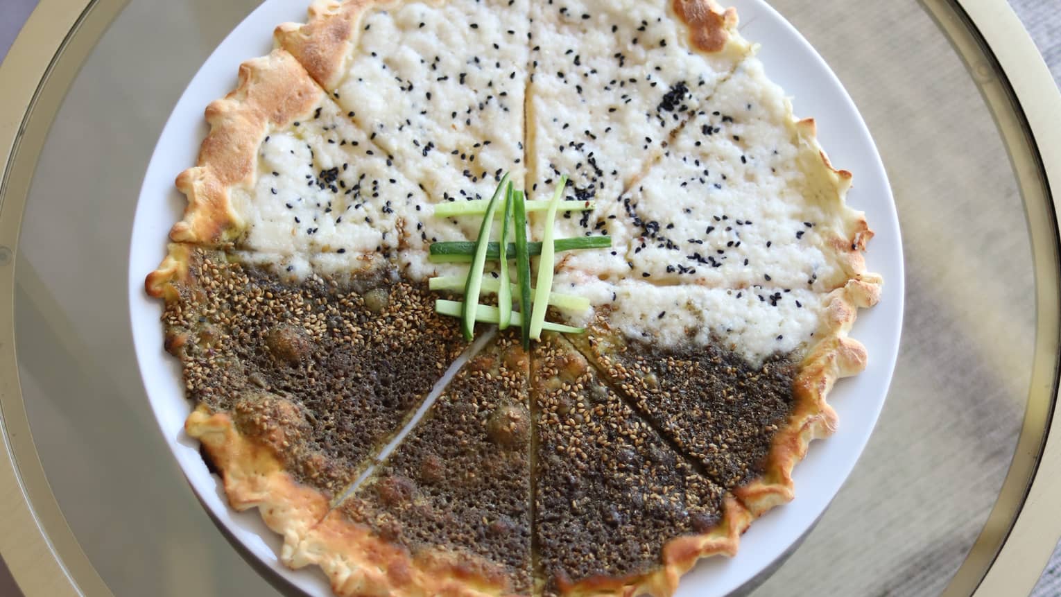 Cheese Manakeesh with crimped edges on round white plate on round glass table