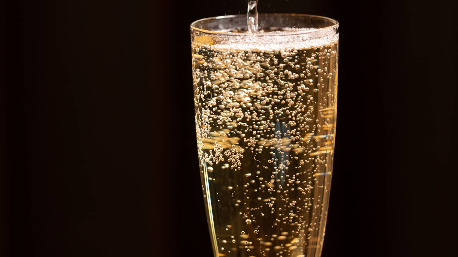 A bottle of champagne is poured into a glass as bubbles float to the top